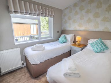 A bedroom with two single beds a bedside table with a lamp and a window at 40 Delamere Point in Delamere