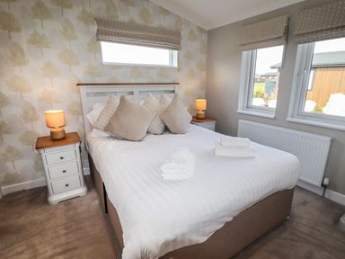 A bedroom with a double bed with pillows and folded towels on it two bedside tables with lamps and windows with patterned blinds at 40 Delamere Point in Delamere