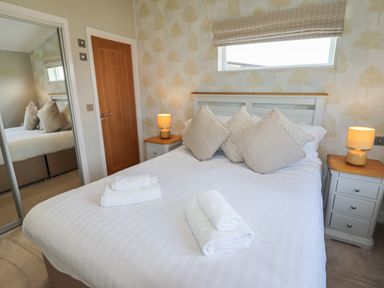 A bedroom with a bed with pillows and folded towels bedside tables with lamps a door and a mirrored wardrobe at 40 Delamere Point in Delamere