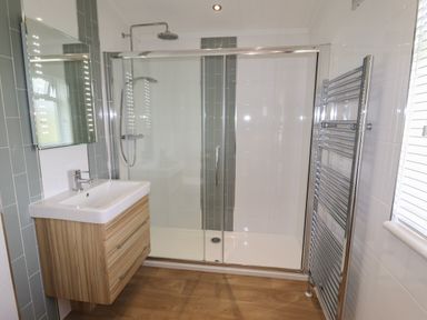 A bathroom with a wooden vanity sink unit a glass door shower and a chrome towel radiator at 40 Delamere Point in Delamere