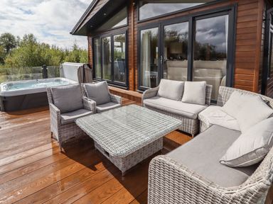 An outdoor deck with wicker sofas, chairs, and a table next to a hot tub at 40 Delamere Point in Delamere