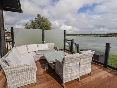 An outdoor deck with wicker seating and a glass table overlooking a lake at 40 Delamere Point in Delamere