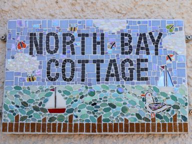 A mosaic sign with text north bay cottage decorated with sailboats birds and bees at North Bay Cottage in Bridlington