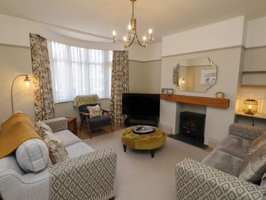 A living room with sofas chairs a round ottoman fireplace and a television at North Bay Cottage in Bridlington