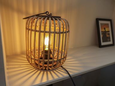 A lit lamp with a wooden cage design on a white surface with a framed photo in the background at North Bay Cottage in Bridlington