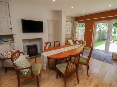 A dining room with a wooden table and six chairs near a wall-mounted television and sliding glass doors at North Bay Cottage in Bridlington