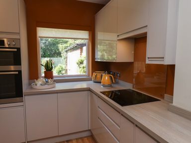 A kitchen with white cabinets orange walls a window a kettle a toaster and an electric stove at North Bay Cottage in Bridlington
