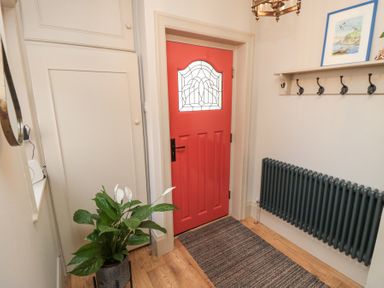 An entryway with a red door a plant on the left a black radiator on the right and a wall-mounted coat rack at North Bay Cottage in Bridlington