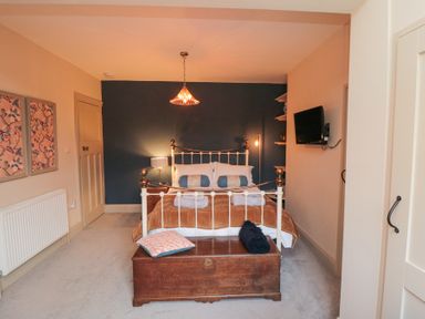 A bedroom with a bed with pillows and blankets a wooden chest at the foot of the bed a wall-mounted television and two framed pictures on the wall at North Bay Cottage in Bridlington