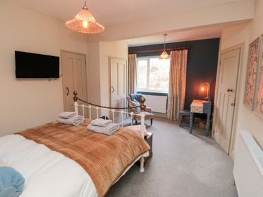 A bedroom with a bed a television an armchair a desk and a window at North Bay Cottage in Bridlington