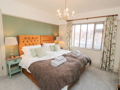 A bedroom with a double bed bedside tables two lamps a window with floral curtains and a chandelier at North Bay Cottage in Bridlington