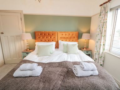 A bedroom with a double bed brown blankets white towels bedside tables with lamps and floral curtains at North Bay Cottage in Bridlington