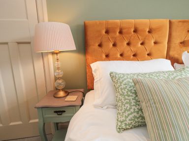 A bedside table with a lamp next to a bed with pillows and an orange upholstered headboard at North Bay Cottage in Bridlington
