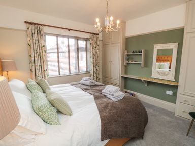 A bedroom with a bed with pillows and folded towels a window with floral curtains built-in wardrobes and a wall mirror at North Bay Cottage in Bridlington
