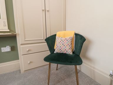 A green chair with a yellow blanket and patterned cushion in a room with beige wardrobe and green wall at North Bay Cottage in Bridlington