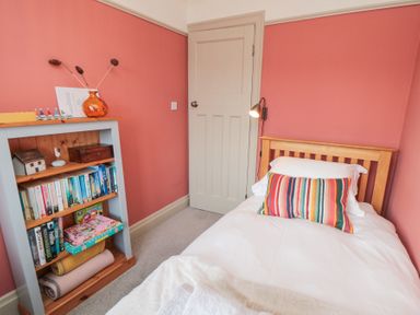 A small bedroom with a single wooden bed with a striped pillow and a bookshelf with books and toys at North Bay Cottage in Bridlington