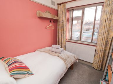 A small bedroom with a single bed with white bedding and a striped pillow near a window with yellow patterned curtains at North Bay Cottage Bridlington