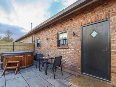 An outdoor patio with a black door, two windows, a wood hot tub, and a small table with two chairs at Robins Nest in Pocklington