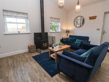 A living room with two blue sofas a wooden coffee table a wood stove and two windows at Robins Nest in Pocklington
