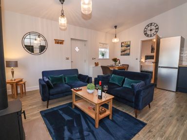 A living room with two blue sofas around a wooden coffee table with wine glasses and a bottle at Robins Nest in Pocklington