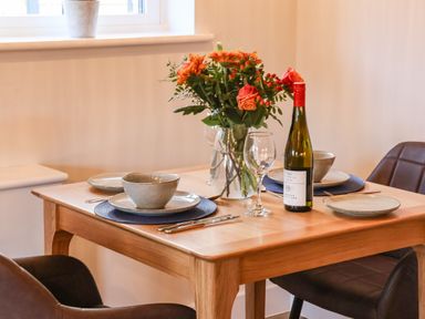 A dining table set with plates bowls cutlery a wine bottle wine glasses and a flower arrangement at Robins Nest in Pocklington