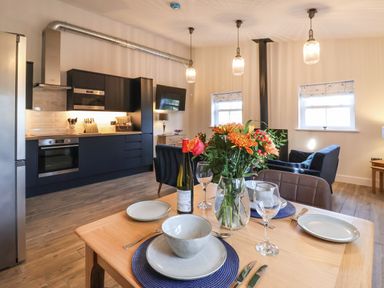 A dining table set with plates and glasses and a kitchen with black cabinets and appliances at Robins Nest in Pocklington