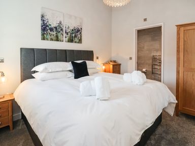 A bedroom with a double bed with white bedding and rolled towels wooden bedside tables and wardrobe at Robins Nest in Pocklington