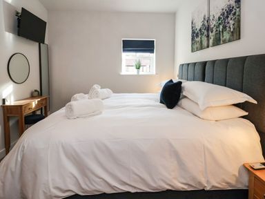 A bedroom with a bed with white linens and pillows a wooden desk with a mirror a wall-mounted television and a window with a plant at Robins Nest in Pocklington