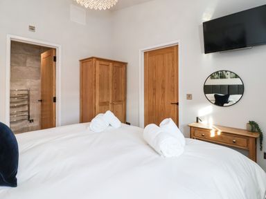 A bedroom with a bed with white sheets and rolled towels a wooden wardrobe wooden doors a small wooden desk a round mirror and a wall mounted television at Robins Nest in Pocklington