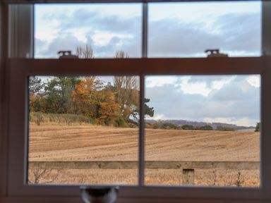 A window view of a harvested field with trees in the background at Robins Nest in Pocklington