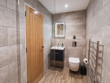 A bathroom with a wooden door a wall-mounted sink and mirror and a wall-mounted toilet at Robins Nest in Pocklington
