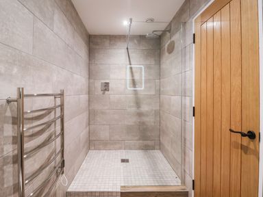 A walk in shower with tiled walls a wooden door and a metal towel rack at Robins Nest in Pocklington