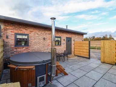A patio with a covered hot tub a small table with two chairs and a brick building at Robins Nest in Pocklington