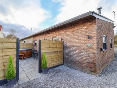 An outdoor patio area with a wooden hot tub and table with chairs next to a brick building at Robins Nest in Pocklington