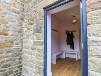 A hallway with wooden floor benches coat hooks and hanging coats at The Coach House in Great Whittington near Corbridge