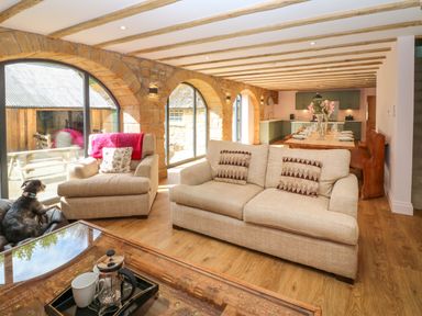 A living room and kitchen with beige sofas a wooden dining table and stone wall arches at The Coach House in Great Whittington near Corbridge