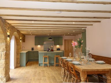 A kitchen with green cabinets and a wooden dining table set with plates and glasses at The Coach House in Great Whittington near Corbridge