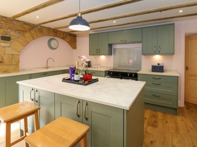 A kitchen with green cabinets a marble countertop an island with stools and a stone arch at The Coach House in Great Whittington near Corbridge