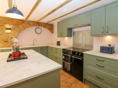 A kitchen with green cabinets a black oven and stone arch at The Coach House Great Whittington near Corbridge