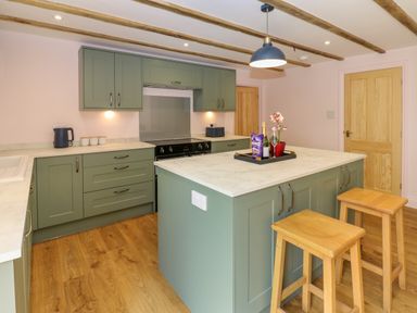 A kitchen with green cabinets a white countertop wooden stools and a wooden floor at The Coach House in Great Whittington near Corbridge