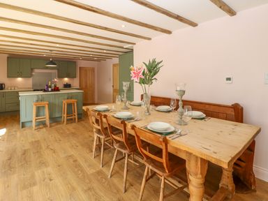 A dining area with a wooden table set with plates glasses and cutlery next to a green kitchen with a wooden floor and ceiling beams at The Coach House in Great Whittington near Corbridge
