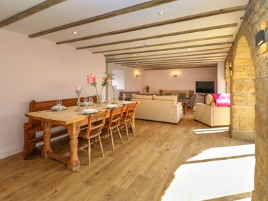 A dining area with a wooden table and chairs next to a living room with sofas and a television at The Coach House in Great Whittington near Corbridge