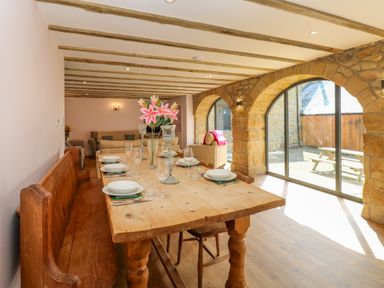 A dining room with a wooden table set with plates and glasses and stone arch windows at The Coach House in Great Whittington near Corbridge