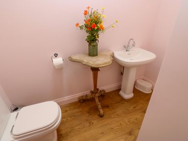 A bathroom with a toilet a sink a small table with a flower vase and wooden floor at The Coach House in Great Whittington near Corbridge