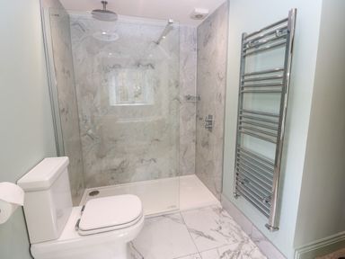 A bathroom with a toilet, a walk-in shower with glass panel, and a wall-mounted towel radiator at The Coach House in Great Whittington near Corbridge