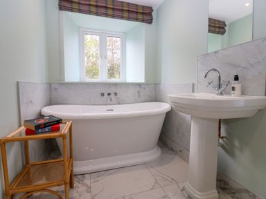A bathroom with a white freestanding bathtub next to a window and a white pedestal sink with a mirror above at The Coach House in Great Whittington near Corbridge