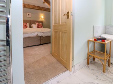A view from a bathroom with a wooden side table and books looking into a bedroom with a bed and pillows at The Coach House in Great Whittington near Corbridge