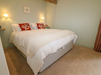 A bedroom with a double bed with white bedding and red pillows two wall lamps and a small framed picture at The Coach House in Great Whittington near Corbridge