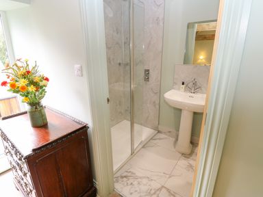 A bathroom with a glass shower enclosure a pedestal sink and a wooden cabinet with flowers at The Coach House Great Whittington near Corbridge