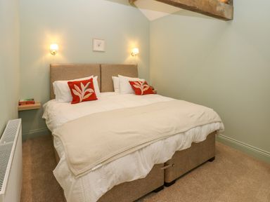A bedroom with a double bed two red pillows two wall lamps and a wooden beam at The Coach House in Great Whittington near Corbridge